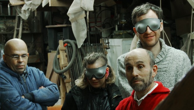 Cette photo représente 4 personnages dans l’atelier d’un sculpteur. Il se dégage de leurs visages une ambiance à la fois joyeuse, accueillante et surprenante. Les personnages semblent nous regarder, mais en fait aucun d’eux ne voit. En effet, deux personnages sont aveugles, les deux autres portent un élégant bandeau sur les yeux.