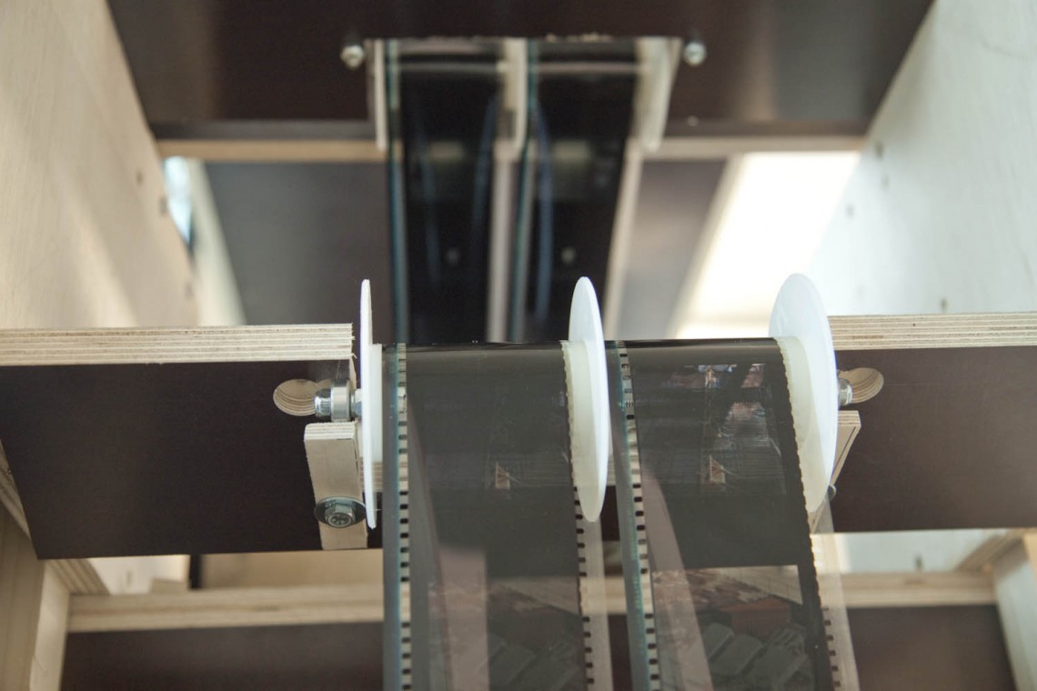 Le 2 fois 8mètres de pellicule cheminent tout autours du cadre. Le glissement des pellicules entre les flasques des poulies est doucement audible par le visiteur. assis.